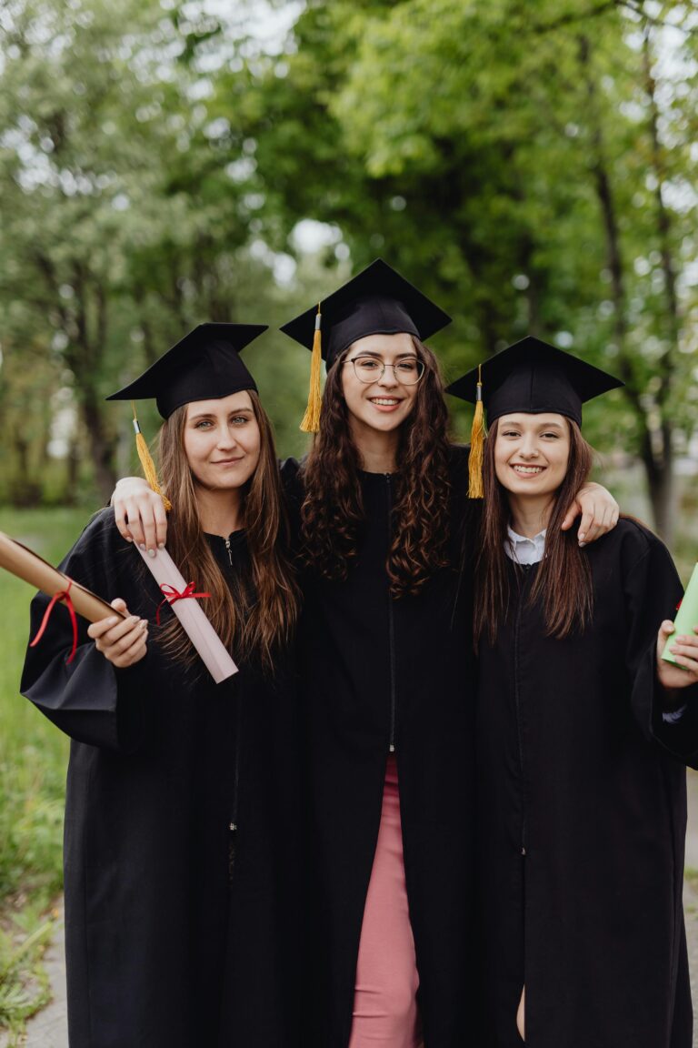 Three female graduates in caps and gowns celebrating their academic success outdoors.